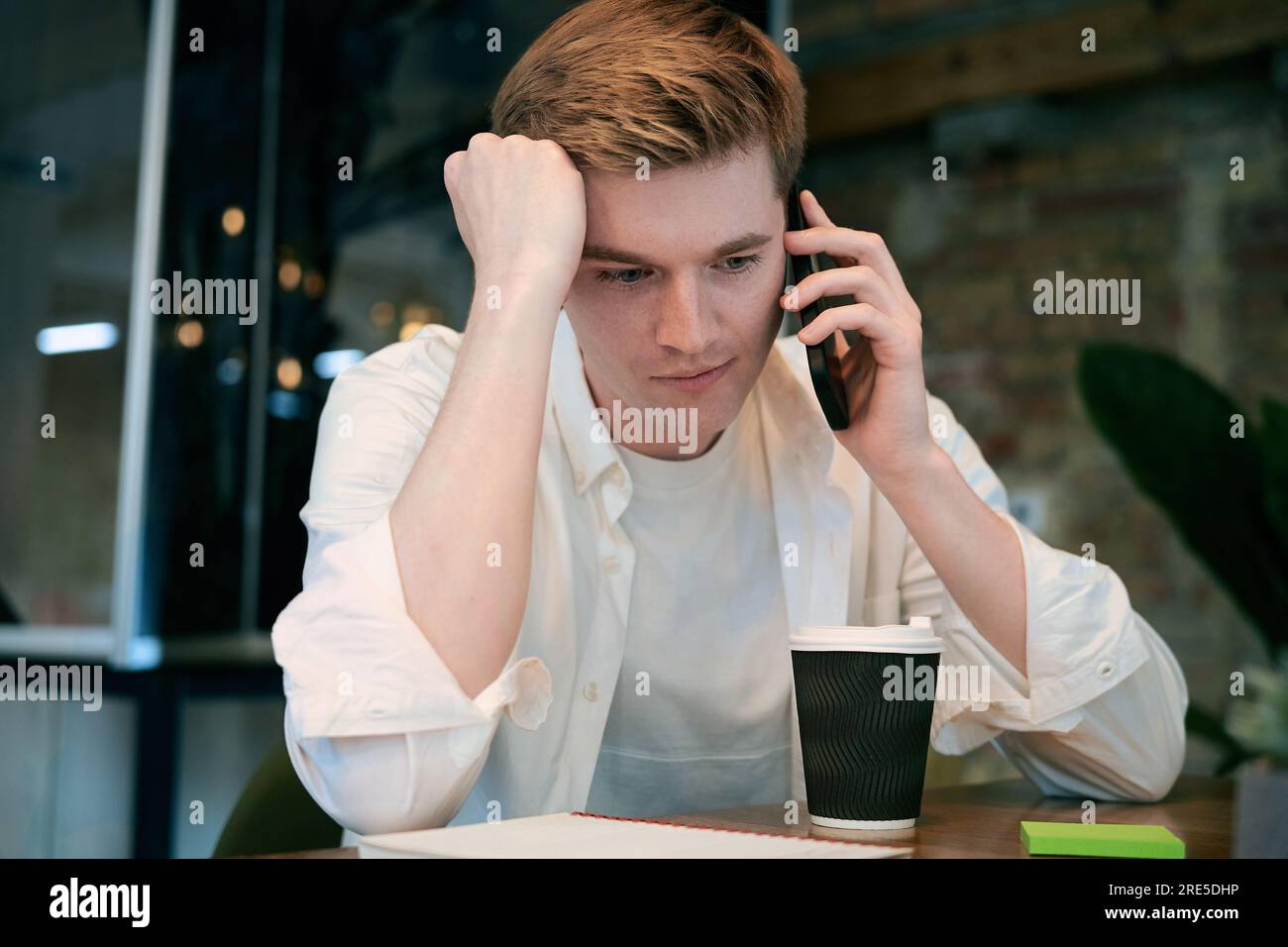 Beschäftigter männlicher Kollege, der ein Smartphone verwendet, während er über Geschäfte spricht, sitzt an seinem Schreibtisch im Büro. Das Konzept der Inbetriebnahme, Zusammenarbeit und Verwaltung Stockfoto