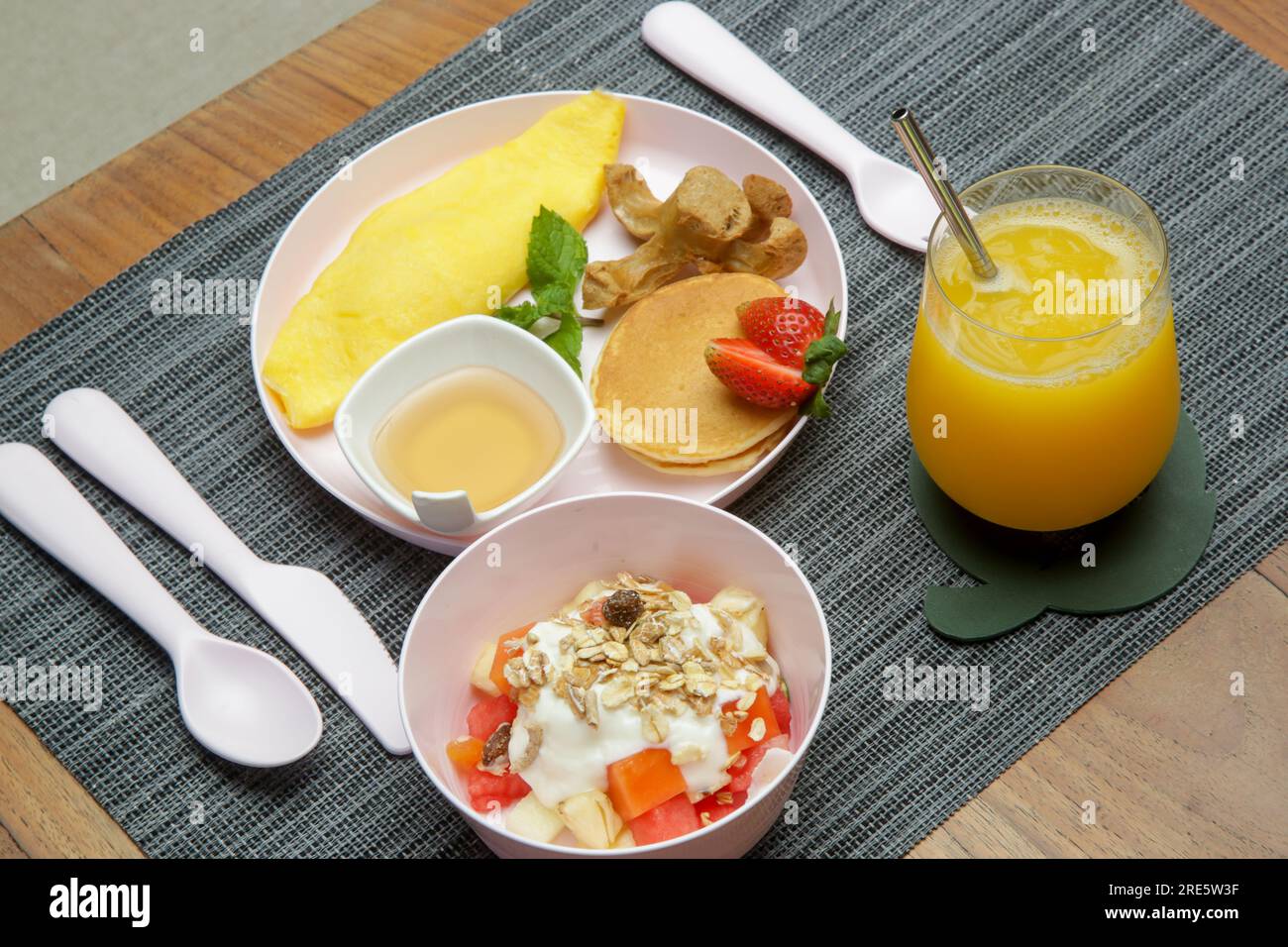Kindermenü - Omelett, Pfannkuchen mit Ahornsirup, Müsli mit Joghurt und ein Glas frisch gepressten Orangensaft auf dem Restauranttisch mit Plastik Stockfoto