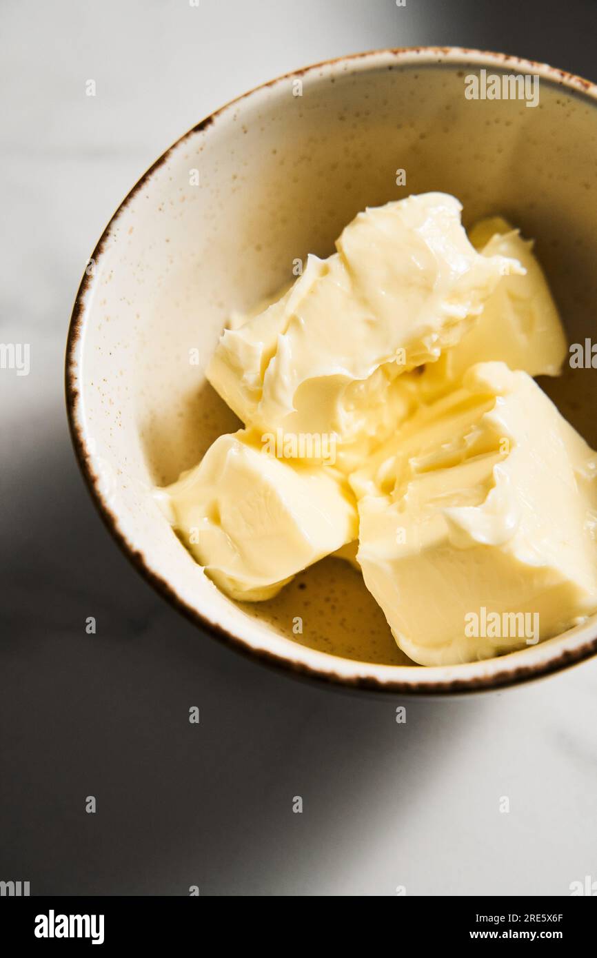 Ungesalzene Butterwürfel in weißer Schüssel auf weißem Marmorhintergrund. Das Öl hat Raumtemperatur, ist weich und flauschig. Stockfoto