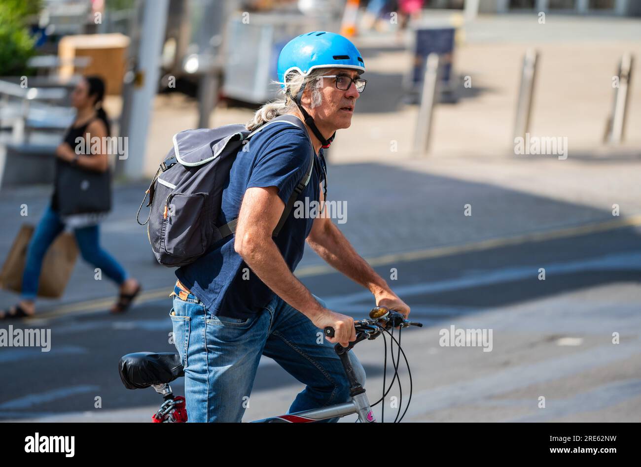 Ein Mann mittleren Alters und Radfahrer, der im Sommer in Großbritannien mit Helm und Rucksack auf einem Fahrrad fährt. Stockfoto