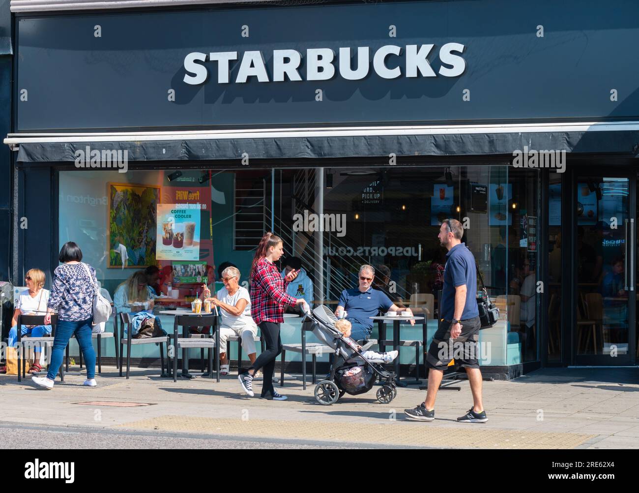Personen, die im Sitzbereich im Freien vor einem Starbucks Coffee Shop in Brighton & Hove, East Sussex, England, Großbritannien, sitzen. Stockfoto