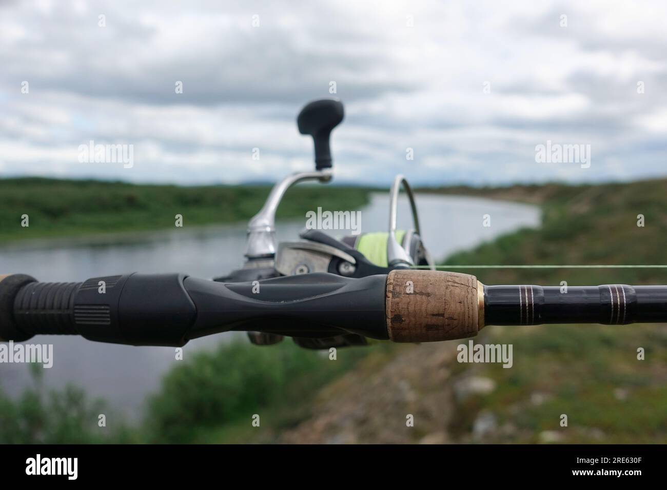 Angelrute und -Rolle am Lainio River im schwedischen Lappland am bedeckten Sommertag. Stockfoto