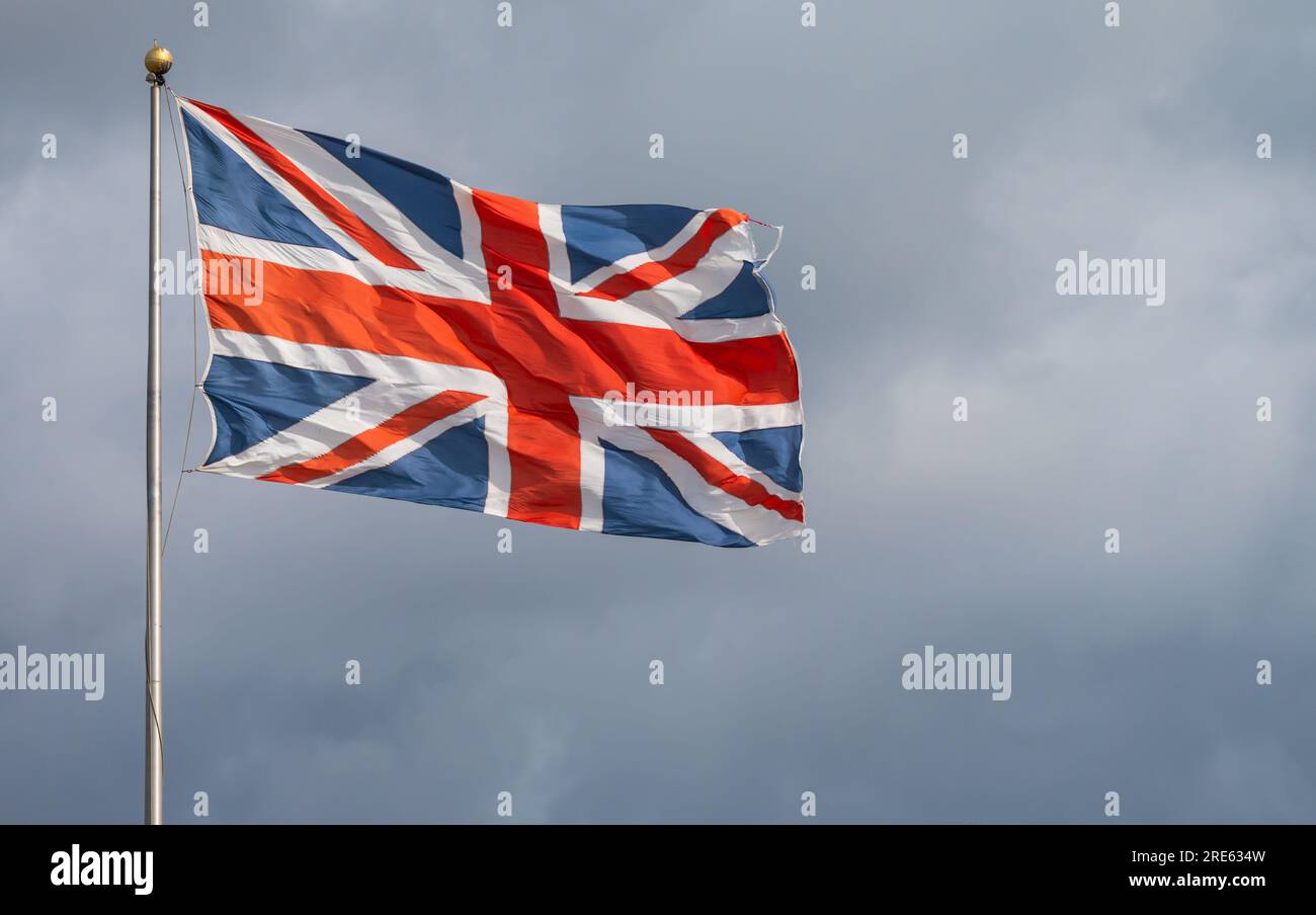 Union Jack, Flagge des Vereinigten Königreichs Großbritannien und Nordirland, fliegt im starken Wind auf einem Stab gegen bewölkten Himmel. Stockfoto