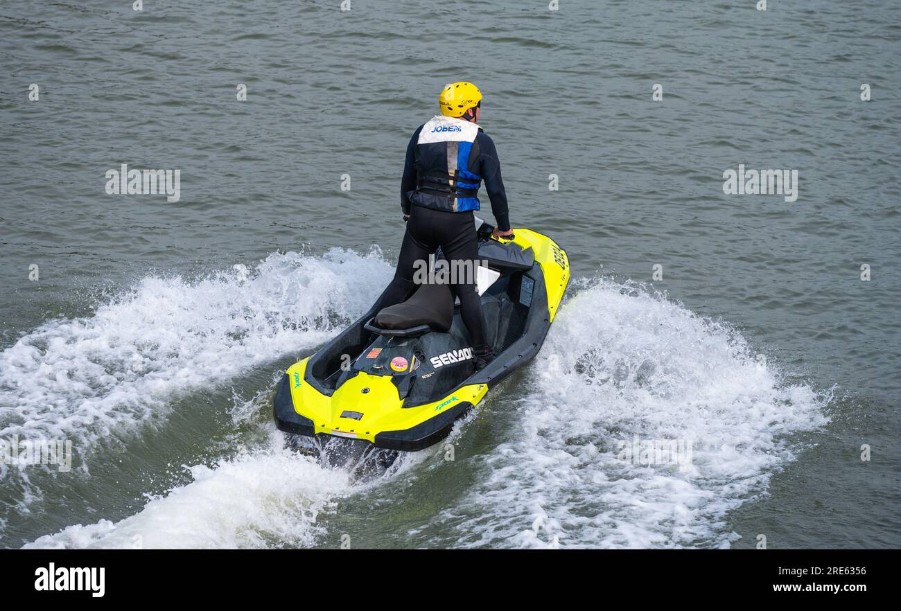 Person, die auf dem Jetski steht, ziemlich langsam auf einem Fluss fährt, nachdem sie auf See Jetski gefahren hat, im Sommer, Großbritannien. Stockfoto