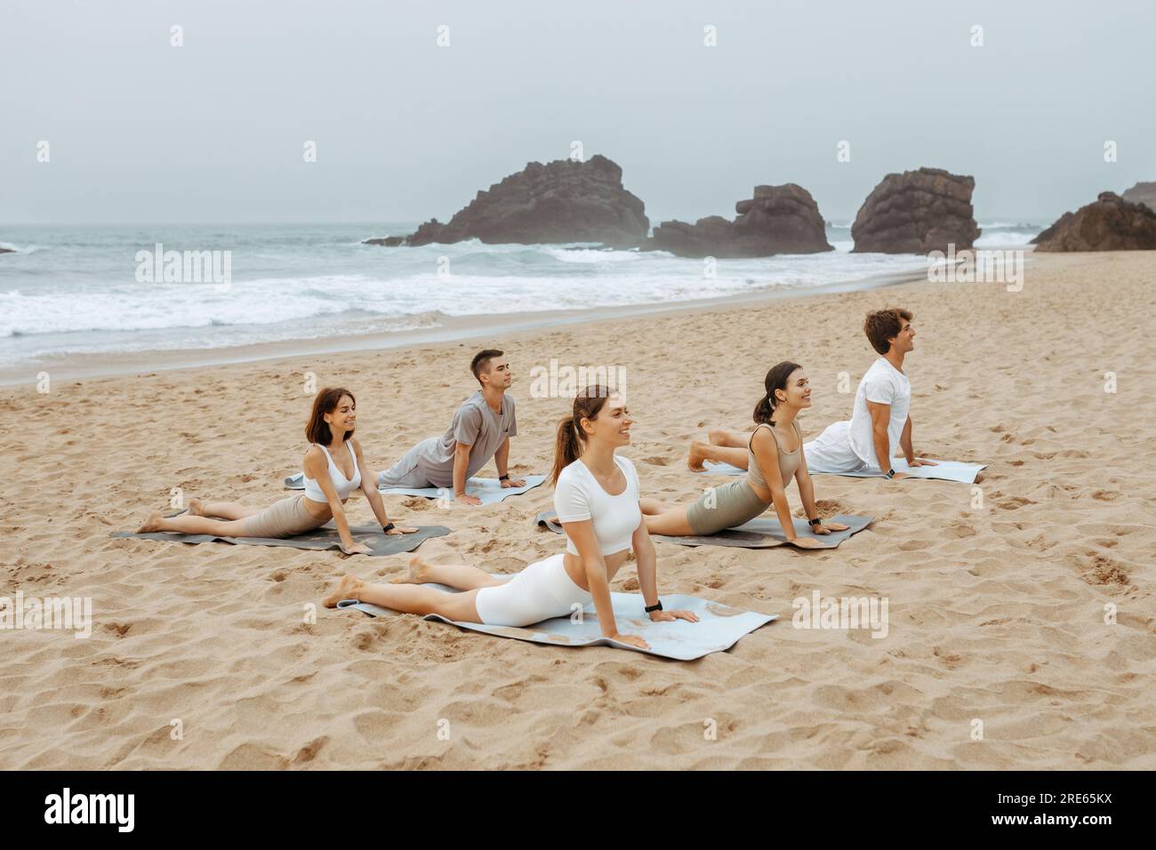 Gezeitenruhe. Gruppe junger Männer und Frauen, die Yoga üben, Kobra auf Matten posieren und am Strand trainieren Stockfoto