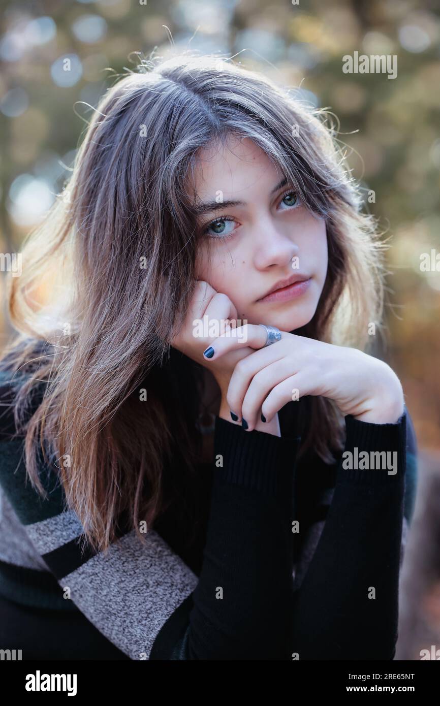 Wunderschöne braune junge Frau, die leider in die Kamera schaut, umgeben von Herbstfarben im Freien. Selektiver Fokus mit unscharfem Hintergrund. Stockfoto