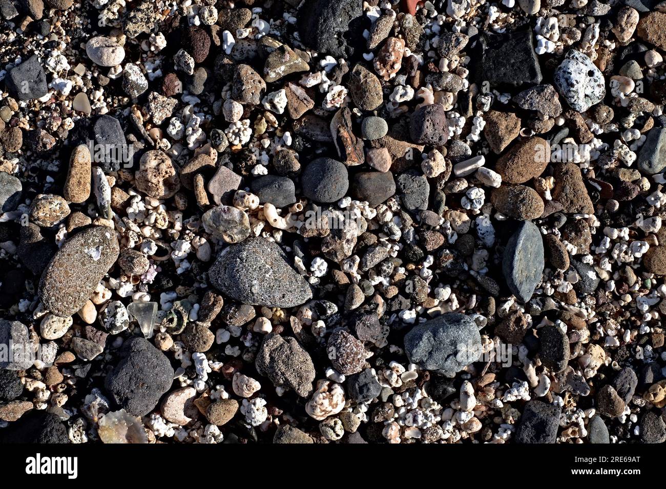 Muster aus verschiedenen weißen, grauen und schwarzen Strandsteinen, Bild mit geringem Kontrast und geringer Sättigung. Stockfoto