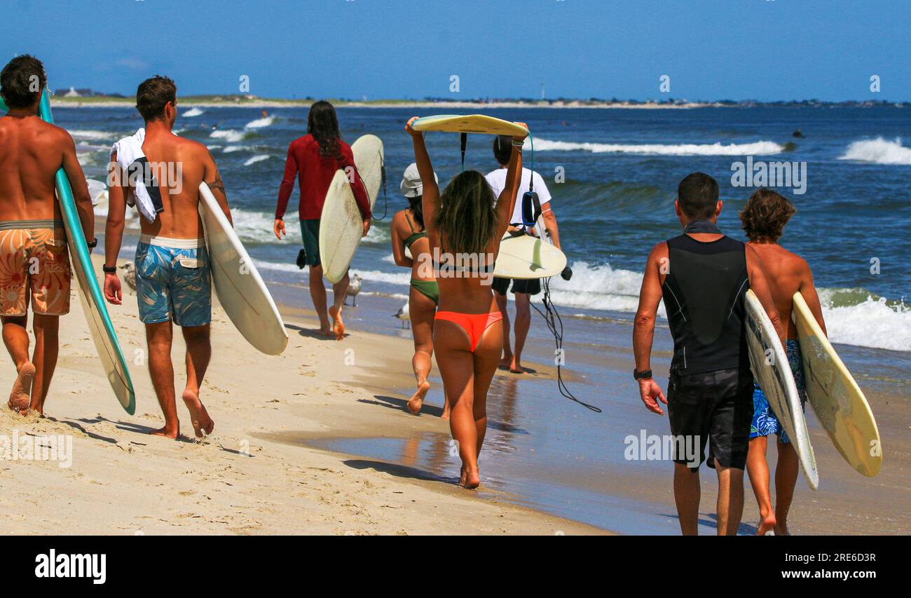 Rückansicht einer Gruppe von Surfern, die den Strand entlang laufen und Surfbretter am Ufer des Gilgo Beach mit sich führen. Stockfoto