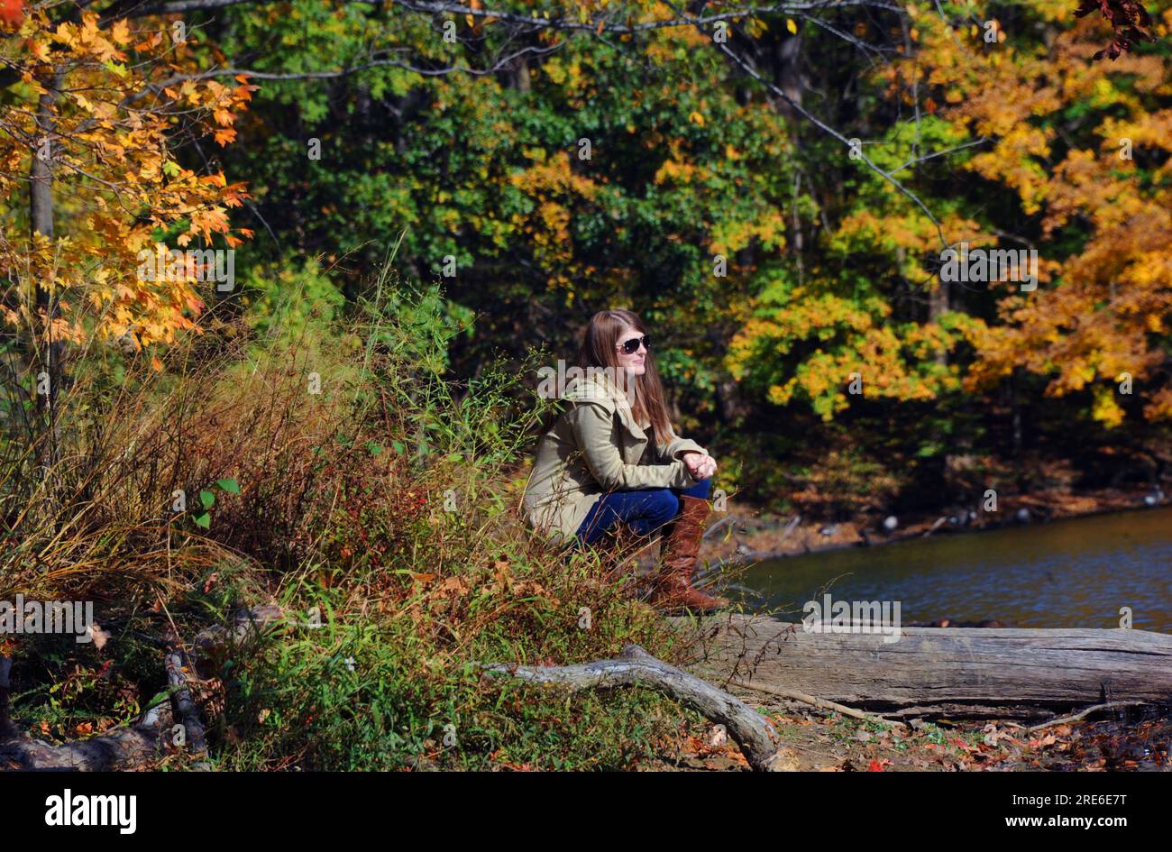 Im Meeman Shelby Forest State Park am Poplar Tree Lake kniet eine attraktive junge Frau still herum. Der Herbst färbt ihre ruhige Welt. Stockfoto