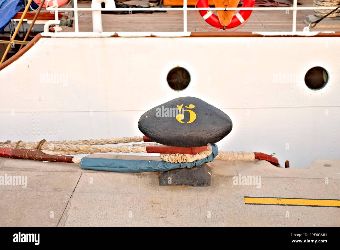 Ein Dock mit einem großen Poller Nummer fünf, Andocklinien und einer weißen Oberseite mit zwei runden Bullaugenfenstern, Details einer Oberseite eines Docks Stockfoto