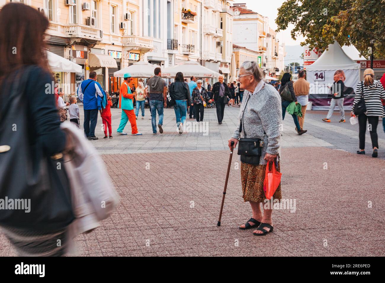 Eine ältere Frau mit Gehstock macht eine Pause in einer von Touristen gefüllten Hauptstraße in Plovdiv, Bulgarien Stockfoto