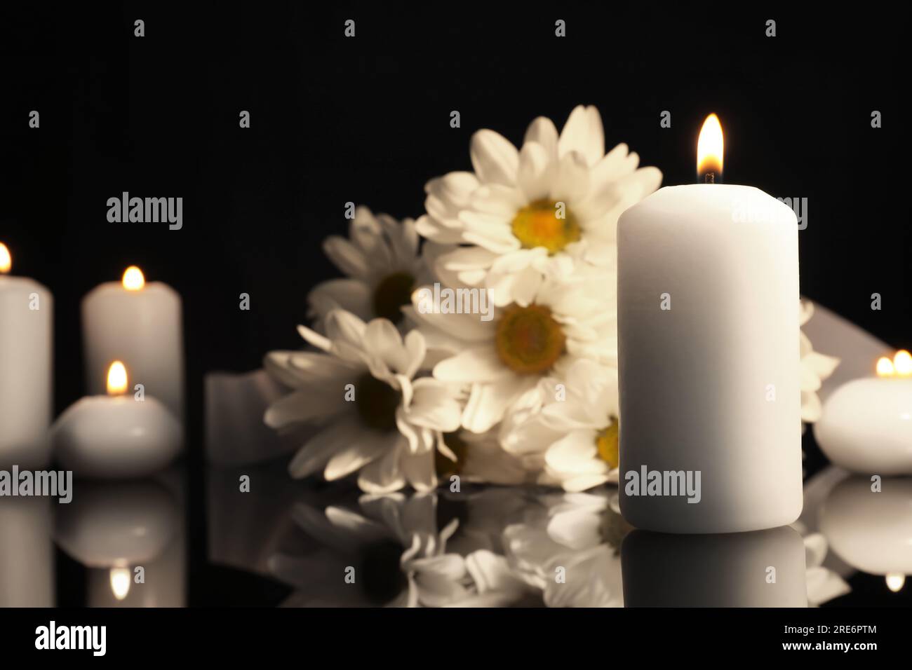 Weiße Chrysanthemen und brennende Kerzen auf schwarzer Spiegeloberfläche in Dunkelheit, Platz für Text. Begräbnissymbole Stockfoto