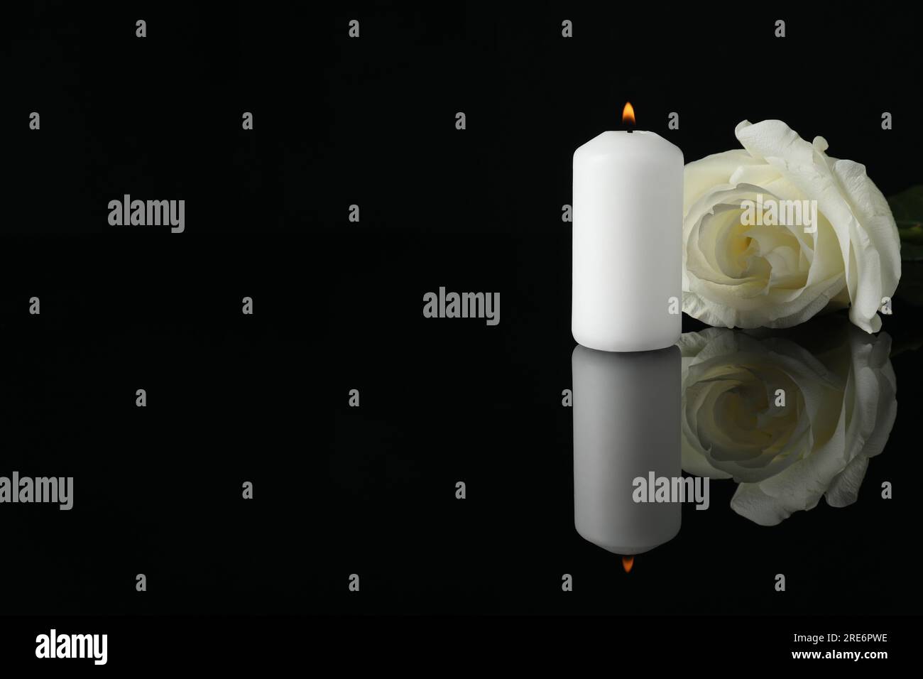 Weiße Rose und brennende Kerze auf schwarzer Spiegeloberfläche bei Dunkelheit, Platz für Text. Begräbnissymbole Stockfoto