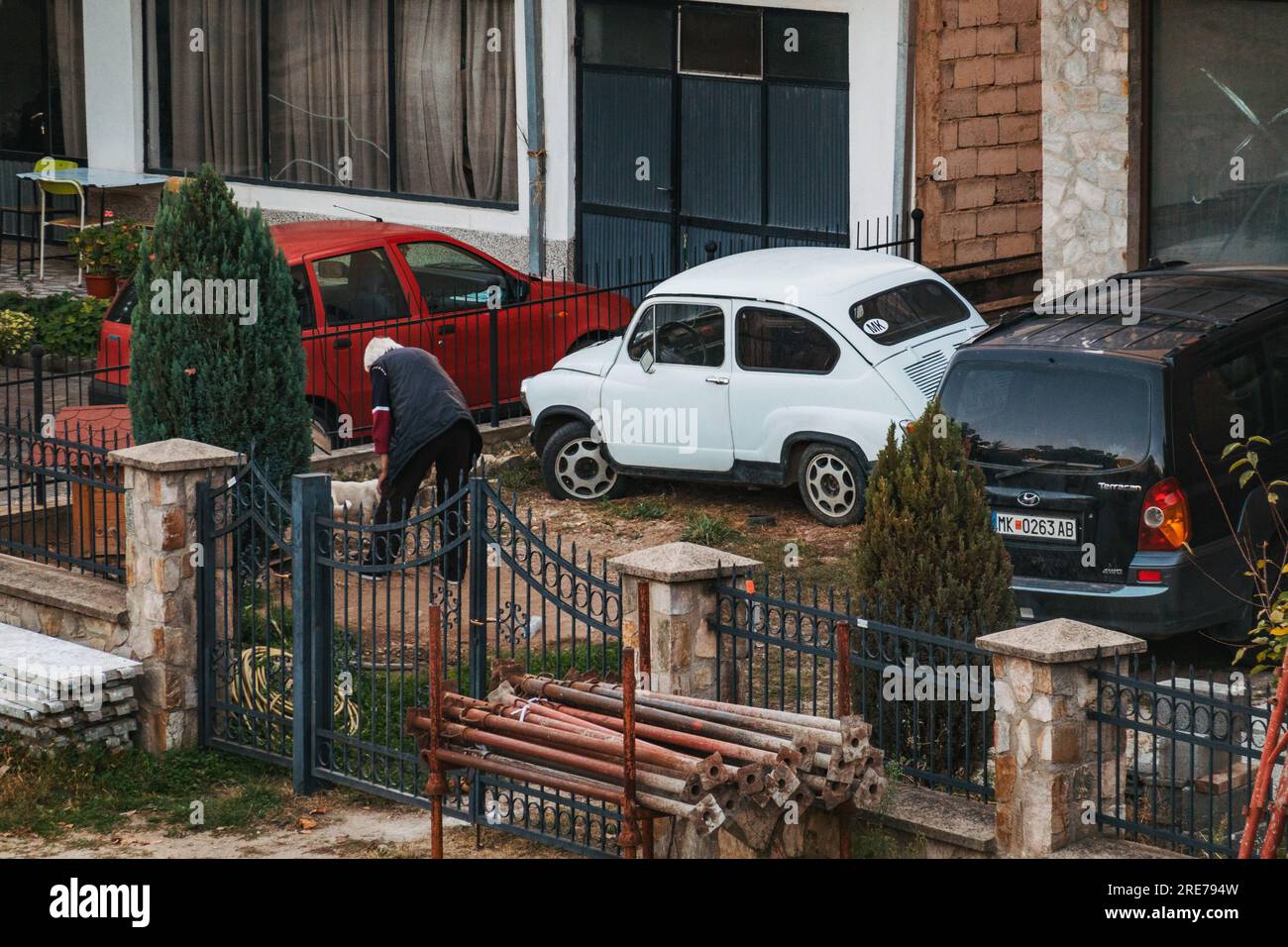 Ein älterer Mann neigt zu seinem Vorhof in der Stadt Makedonska Kamenitsa, Nordmazedonien. Eine weiße Zastava 750 ist davor geparkt Stockfoto