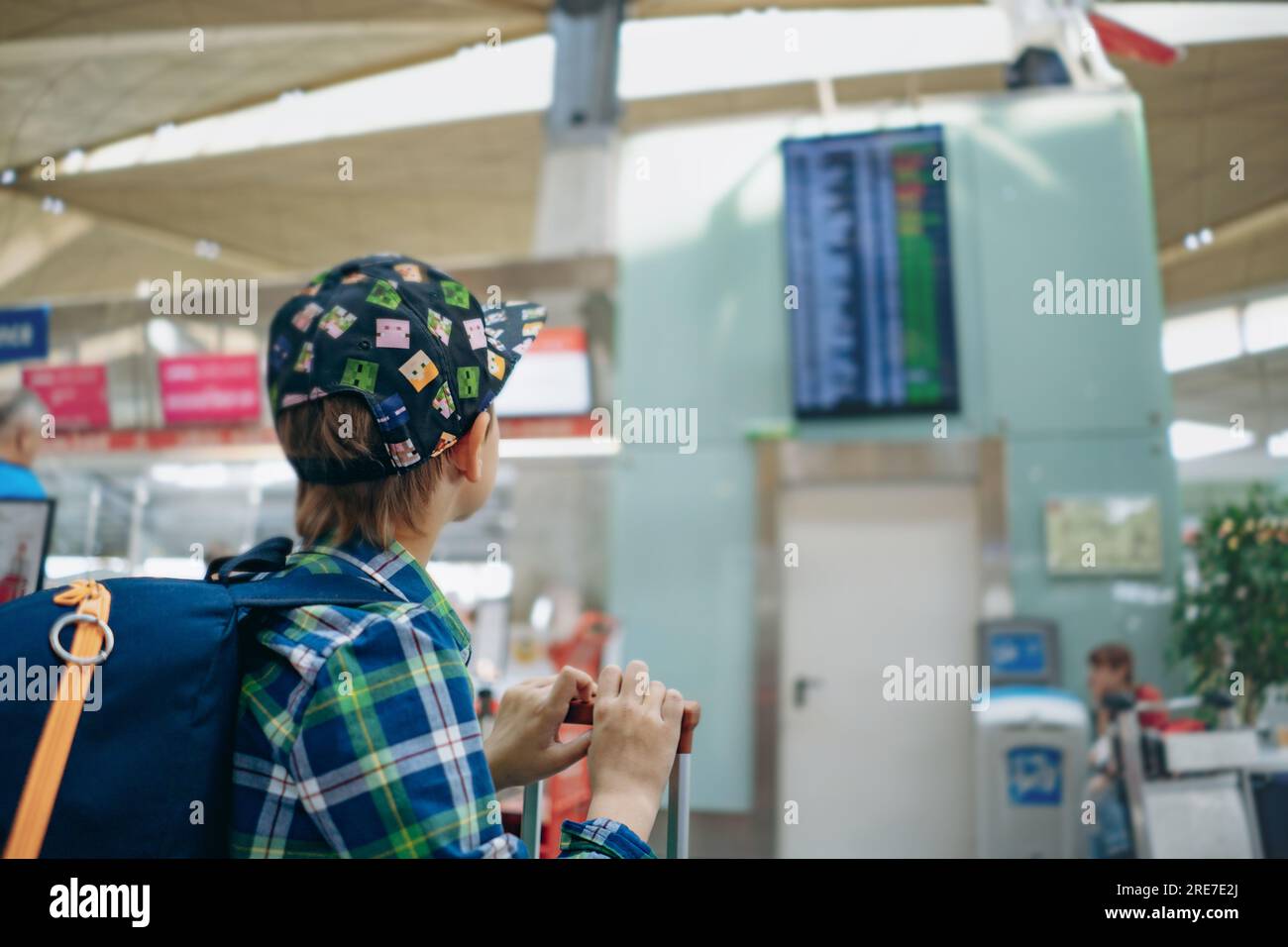 europäischer Junge mit Mütze und Rucksack, der die Flugzeit an der Abflughalle am Flughafen überprüft. Hochwertiges Foto Stockfoto