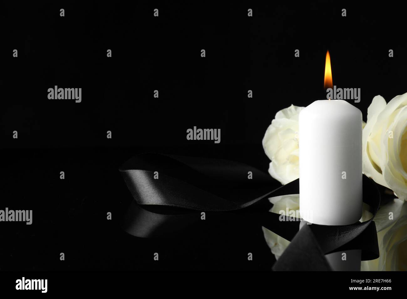 Brennende Kerze, weiße Rosen und Band auf schwarzer Spiegeloberfläche bei Dunkelheit, Nahaufnahme mit Platz für Text. Begräbnissymbole Stockfoto