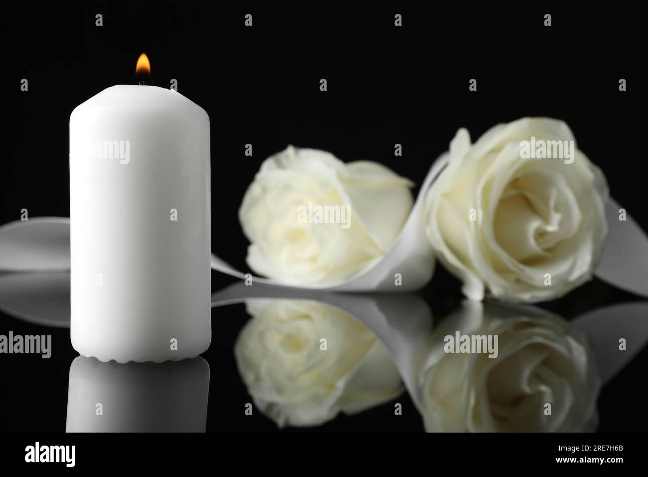 Brennende Kerze, weiße Rosen und Band auf schwarzer Spiegeloberfläche bei Dunkelheit, Nahaufnahme mit Platz für Text. Begräbnissymbole Stockfoto