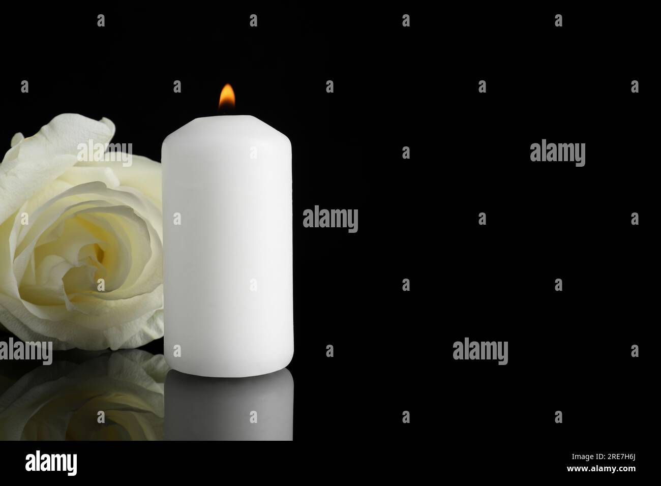 Weiße Rose und brennende Kerze auf schwarzer Spiegeloberfläche bei Dunkelheit, Nahaufnahme mit Platz für Text. Begräbnissymbole Stockfoto