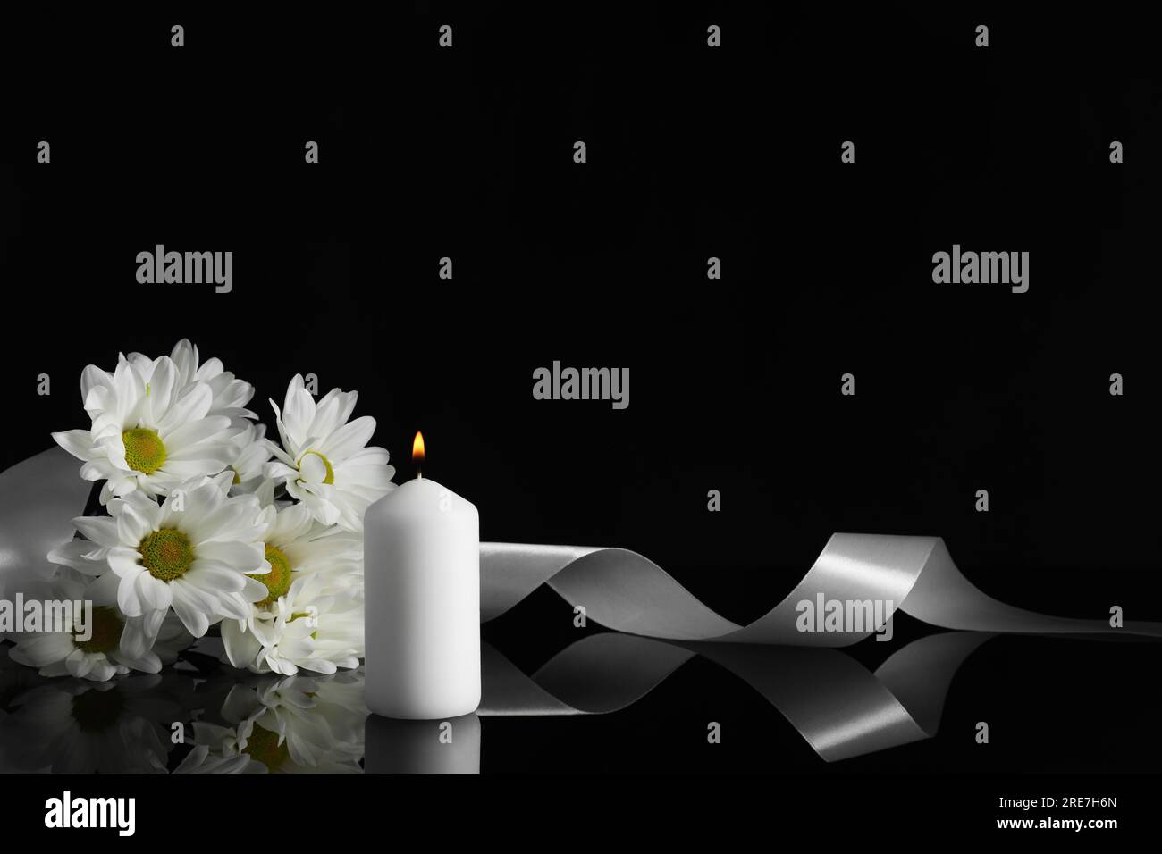 Brennende Kerze, weiße Chrysanthemen und Band auf schwarzer Spiegeloberfläche bei Dunkelheit, Platz für Text. Begräbnissymbole Stockfoto
