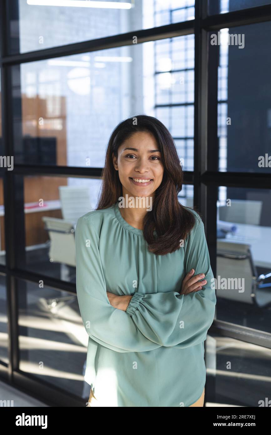 Porträt einer glücklichen, birassischen, lässigen Geschäftsfrau mit langen Haaren und gekreuzten Armen im Amt Stockfoto