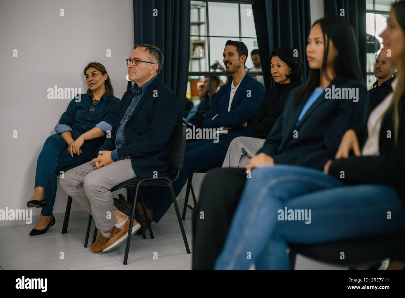 Gruppe von Multiethnen in formeller Kleidung, die an einem modernen Arbeitsplatz auf Stühlen sitzen und während des Seminars aufmerksam wegschauen Stockfoto