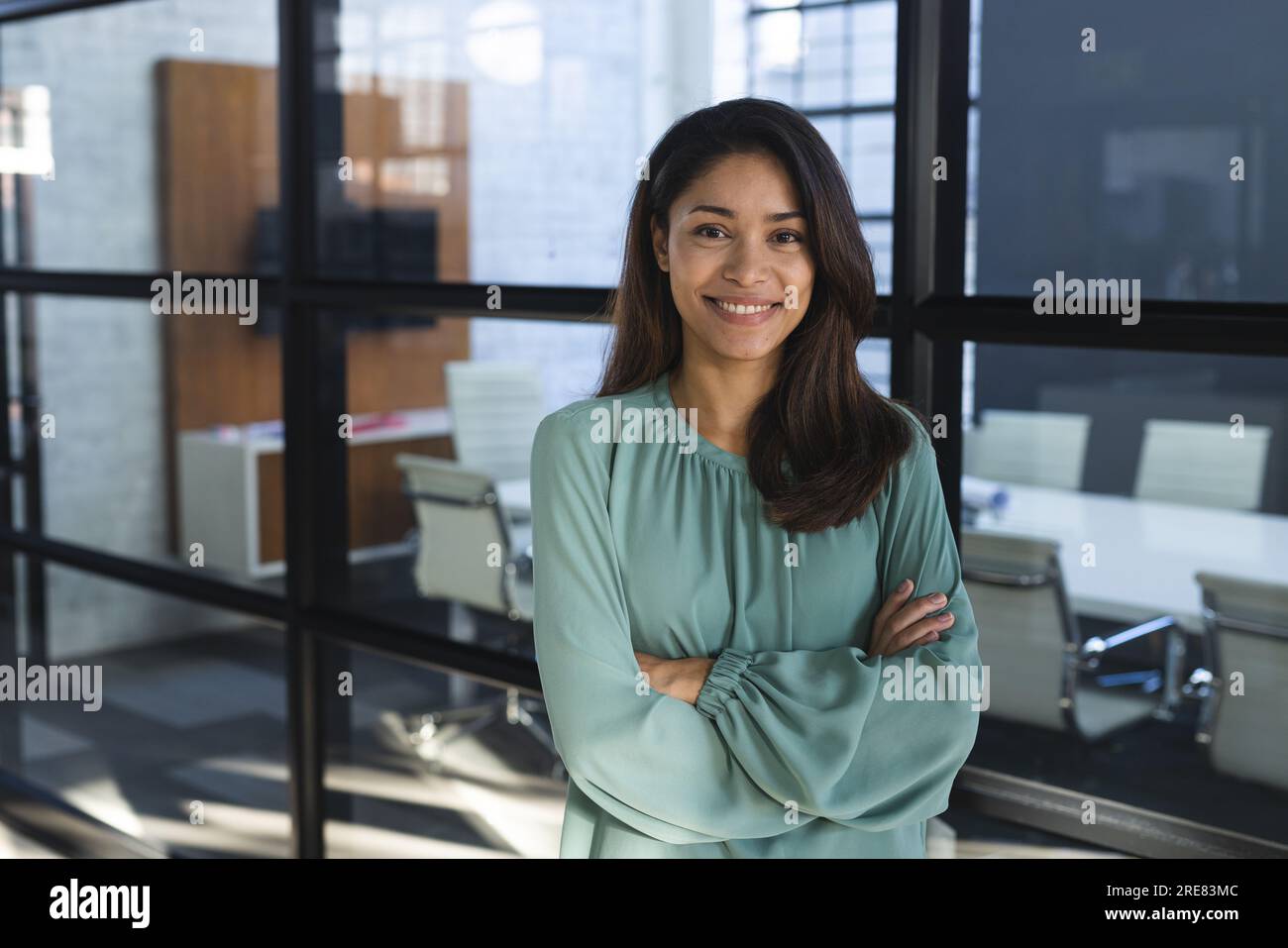 Porträt einer glücklichen, birassischen, lässigen Geschäftsfrau mit langen Haaren und gekreuzten Armen im Amt Stockfoto