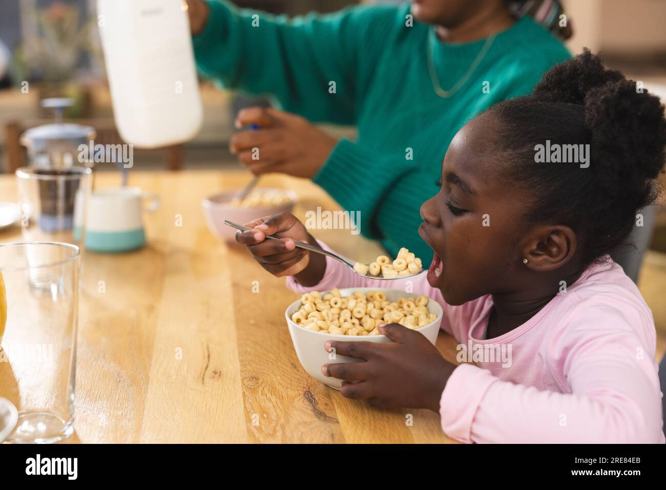 Glückliche afroamerikanische Mutter und Tochter sitzen am Tisch und frühstücken zu Hause Stockfoto