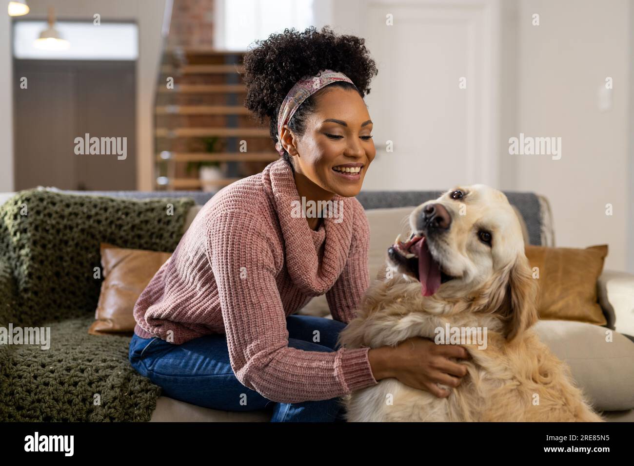 Glückliche, birassische Frau, die zu Hause Hund streichelt Stockfoto