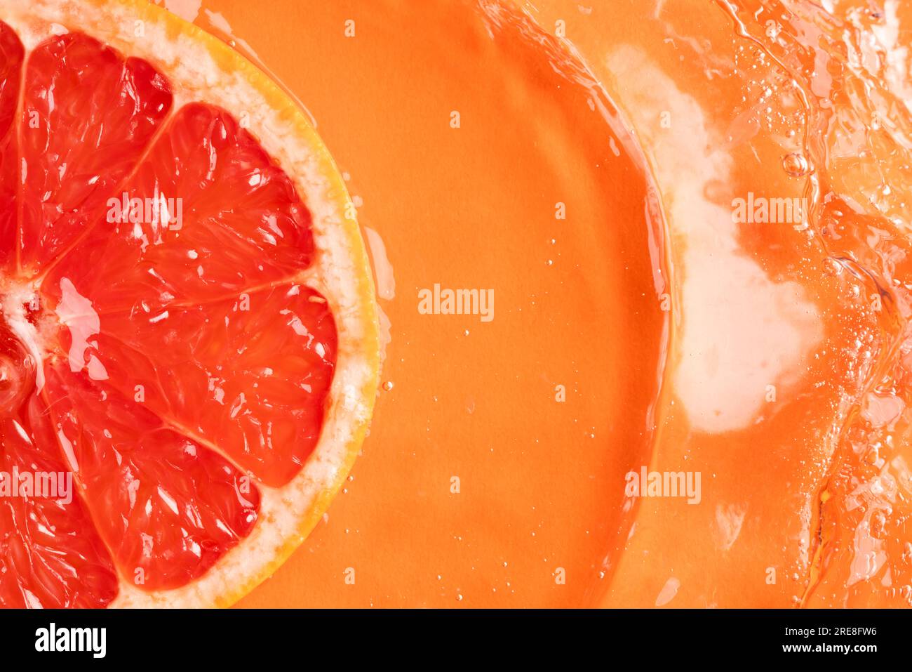 Nahaufnahme einer roten Grapefruitscheibe im Wasser mit Kopierbereich auf orangefarbenem Hintergrund Stockfoto