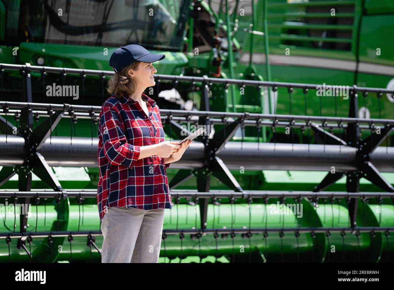 Frau Farmer mit digitalem Tablet auf einem Hintergrund von Harvester. Smart Farming-Konzept. Stockfoto
