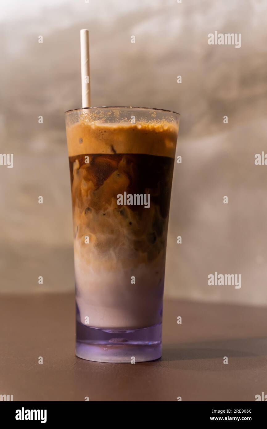 Nahaufnahme eines Eiskaffees in einem hohen Glas mit Sahne und Papierstroh auf einem Holztisch. Stockfoto
