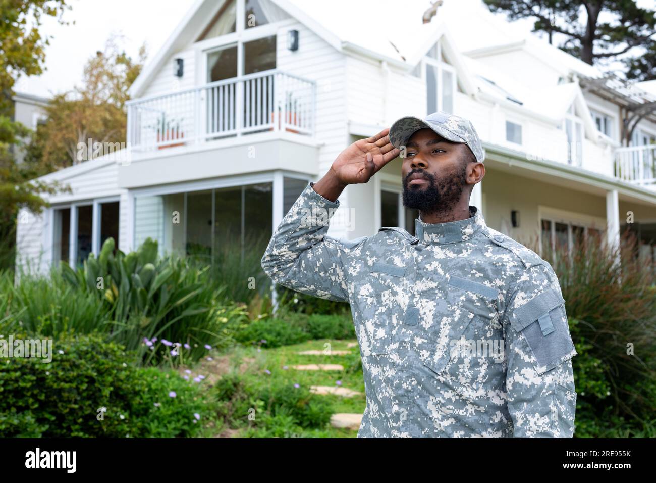 afroamerikanischer Soldat in Militäruniform, salutiert und bleibt gegen das Haus Stockfoto