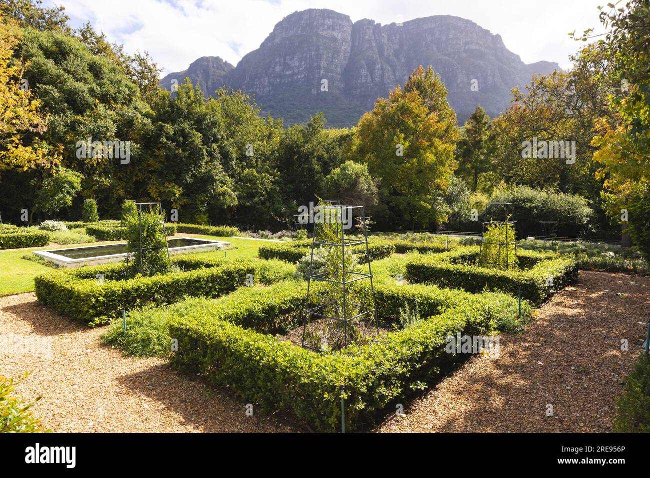 Dekorative Hecken, Schotterwege und Rasen in einem sonnigen formellen Garten mit Bergen dahinter, Kopierraum Stockfoto