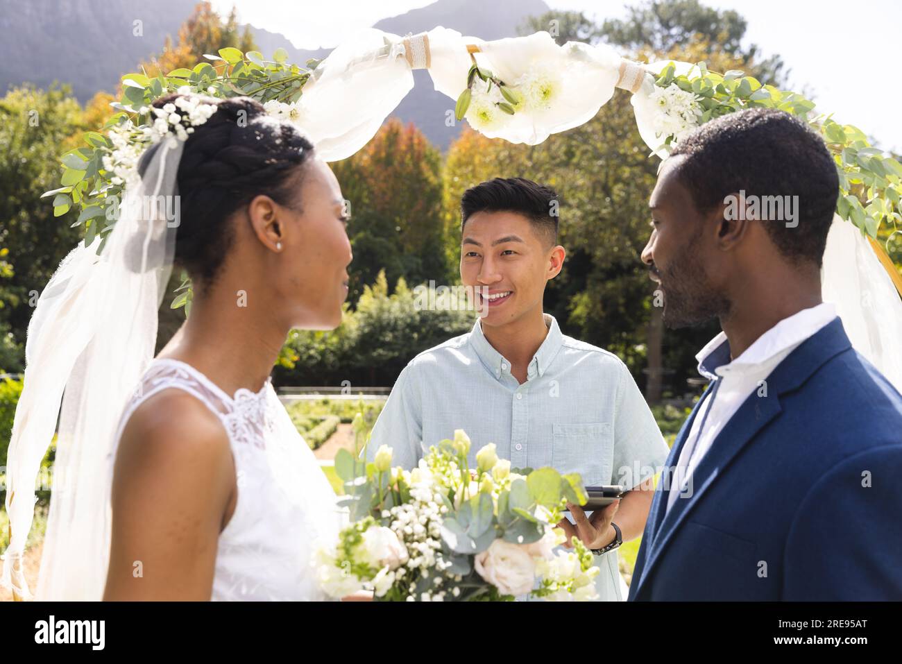 Ein vielseitiger Beamter mit Braut und Bräutigam bei der Hochzeitszeremonie im sonnigen Garten Stockfoto