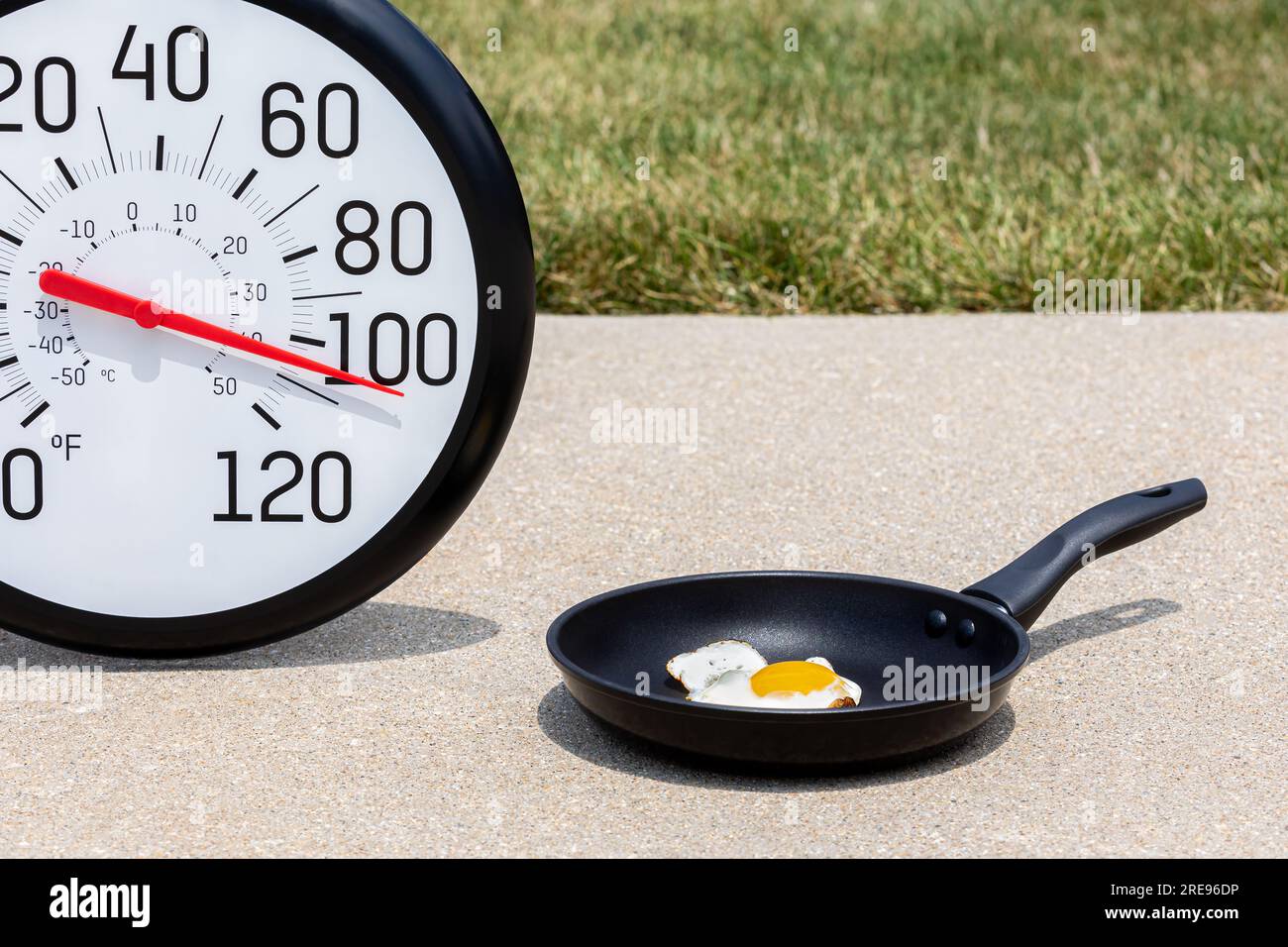 Eierkochen auf Gehweg mit Thermometer in der Sonne während der Hitzewelle. Warn-, Hochtemperatur- und Hitzewarnkonzept. Stockfoto