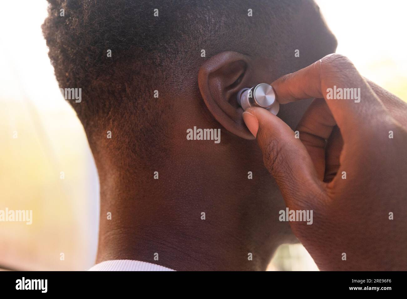 Nahaufnahme von außen: Abgeschnittener, nicht wiedererkennbarer junger afroamerikanischer Mann, der echte kabellose Kopfhörer trägt und draußen Musik hört Stockfoto