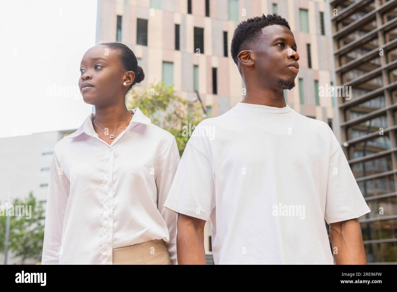 Von unten: Schwarzer Mann in weißem T-Shirt und afroamerikanische Freundin, die auf der Straße der Stadt steht und in verschiedene Richtungen wegschaut Stockfoto