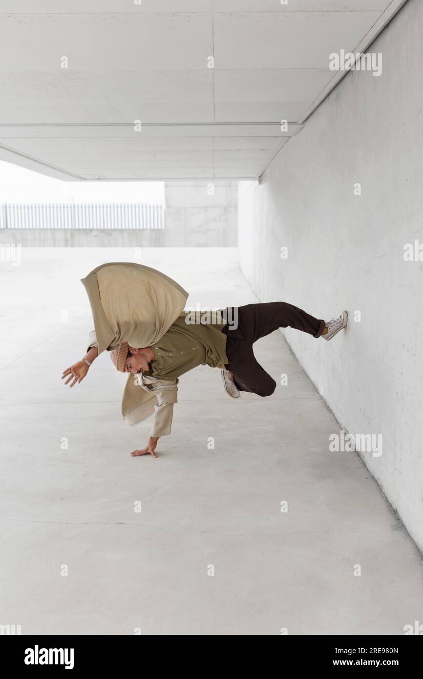 Männliche Tänzerin balanciert auf dem Arm und zeigt Breakdance-Bewegung während Lehnt sich an die Betonwand des Gebäudes in der Stadt Stockfoto