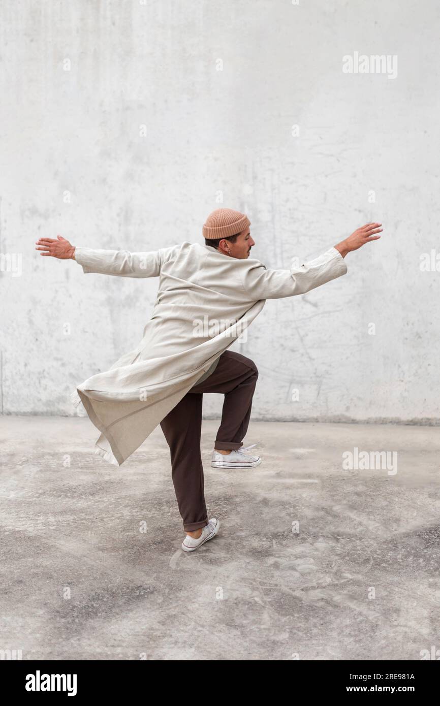 Rückansicht eines anonymen männlichen Breakdancers, der in der Stadt auftrat Bereich in der Nähe der grauen Gebäudewand Stockfoto