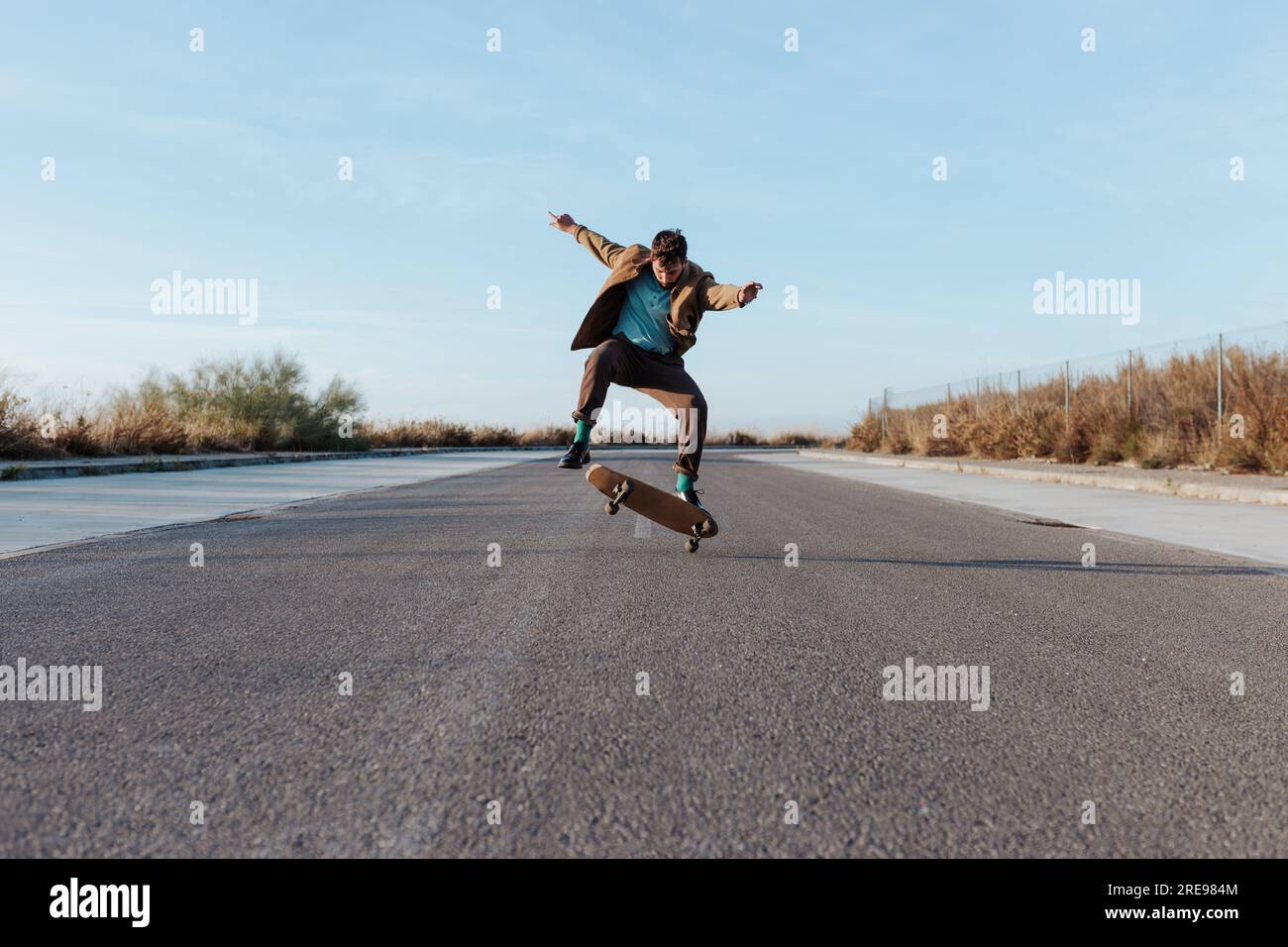 Ganzkörper junge bärtige Skater in casual Outfit springen während Durchführung Kickflip auf Skateboard auf Asphalt Straße Stockfoto