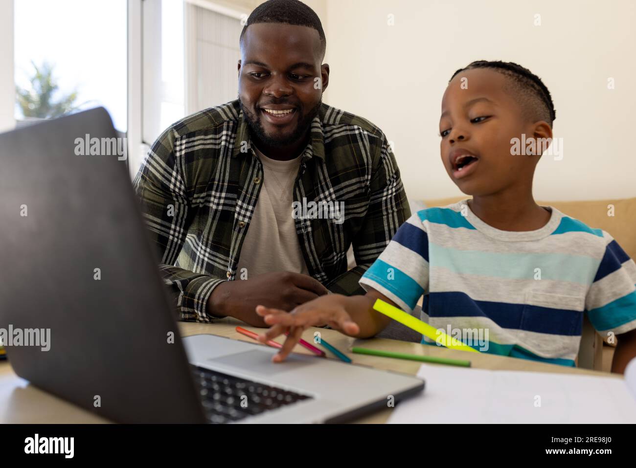 Glücklicher afroamerikanischer Vater und Sohn, der mit dem Laptop sitzt und zusammen Schularbeiten macht Stockfoto