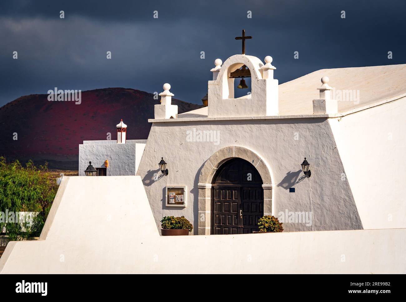 Eine weiß getünchte Kirche auf Lanzarote mit stürmischem Himmel und dem Vulkan Caldera Colorada im Hintergrund Stockfoto