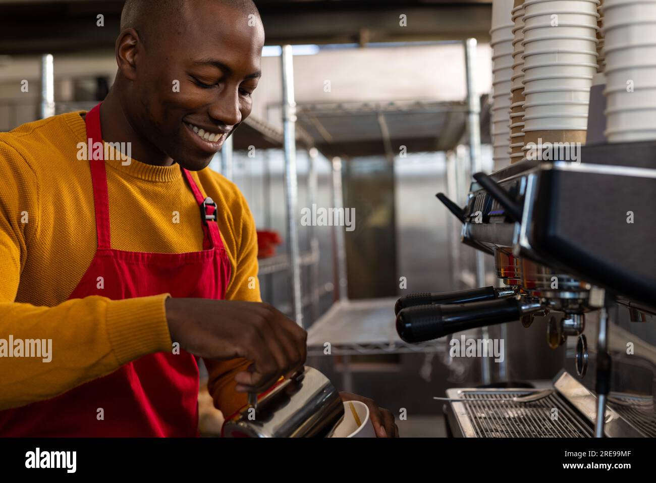 Glücklicher afroamerikanischer Bäckereiarbeiter, der eine rote Schürze trägt und Kaffee zubereitet Stockfoto