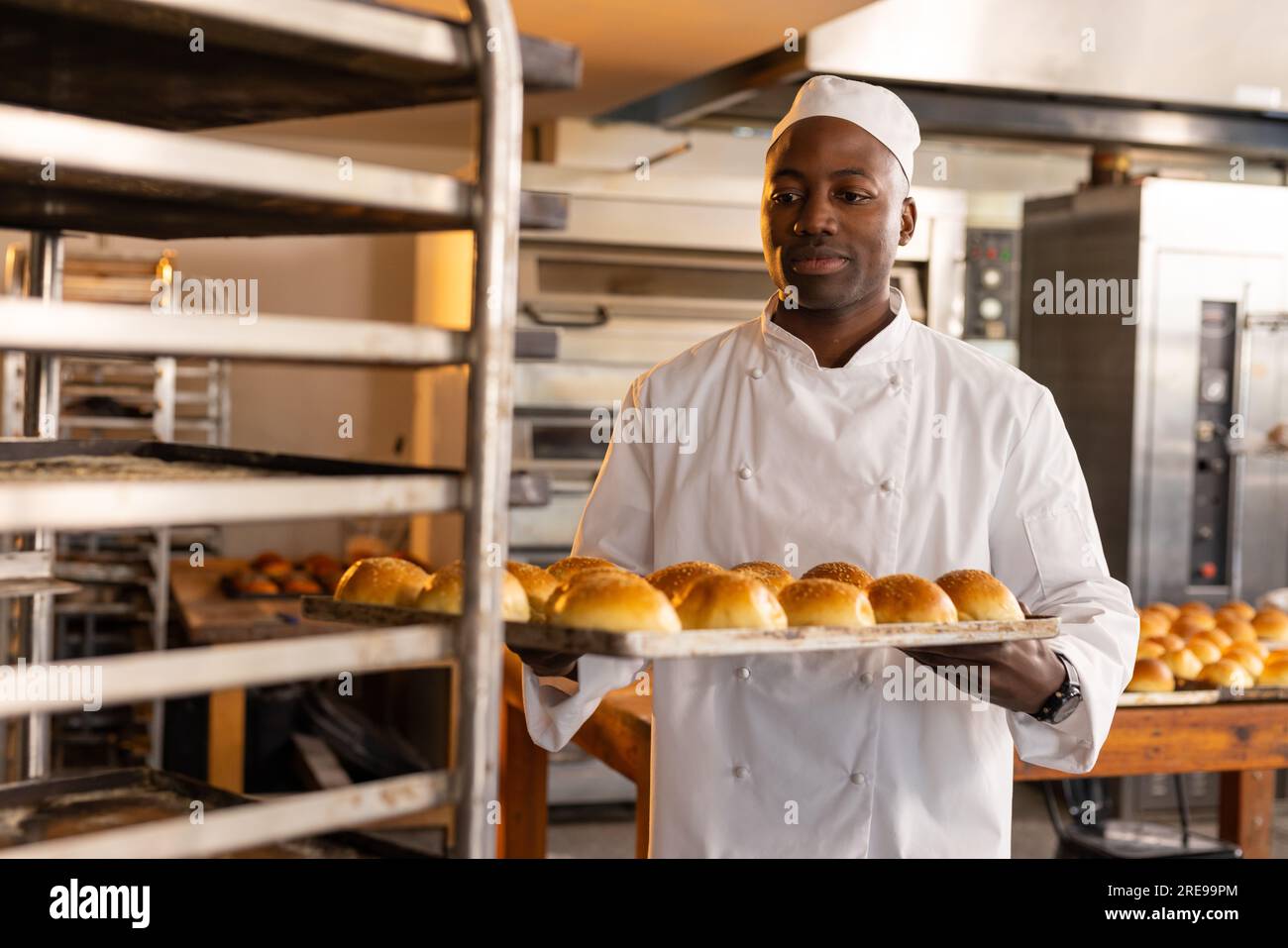 Glücklicher afroamerikanischer Bäcker in der Bäckerei Küche mit Backblech mit frischen Brötchen Stockfoto