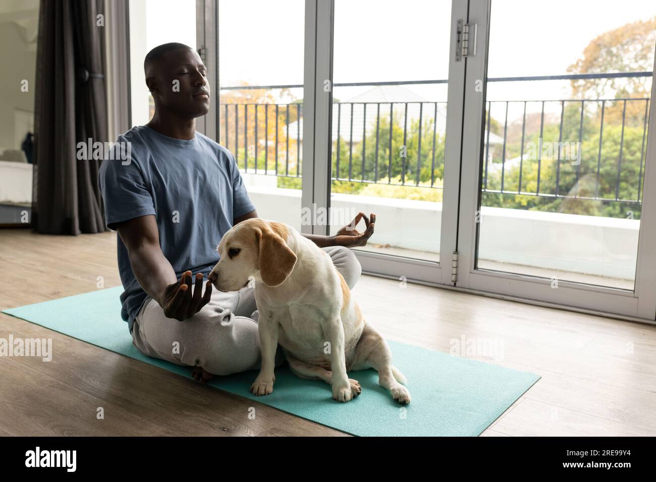 Ein afroamerikanischer Mann, der Yoga macht und meditiert, mit seinem Hund zu Hause Stockfoto