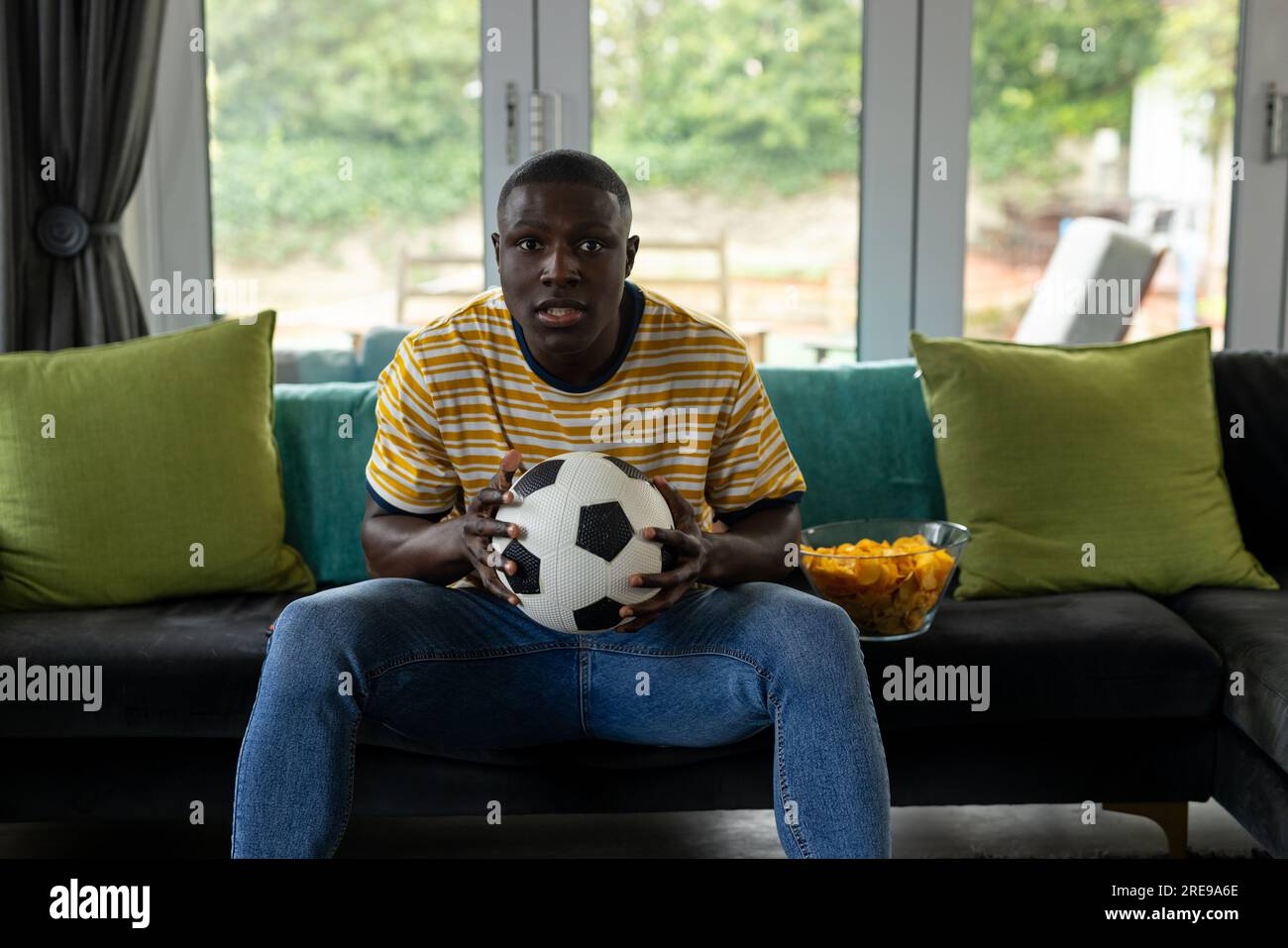 Ein glücklicher afroamerikanischer Mann, der sich das Fußballspiel ansieht und zu Hause unterstützt Stockfoto