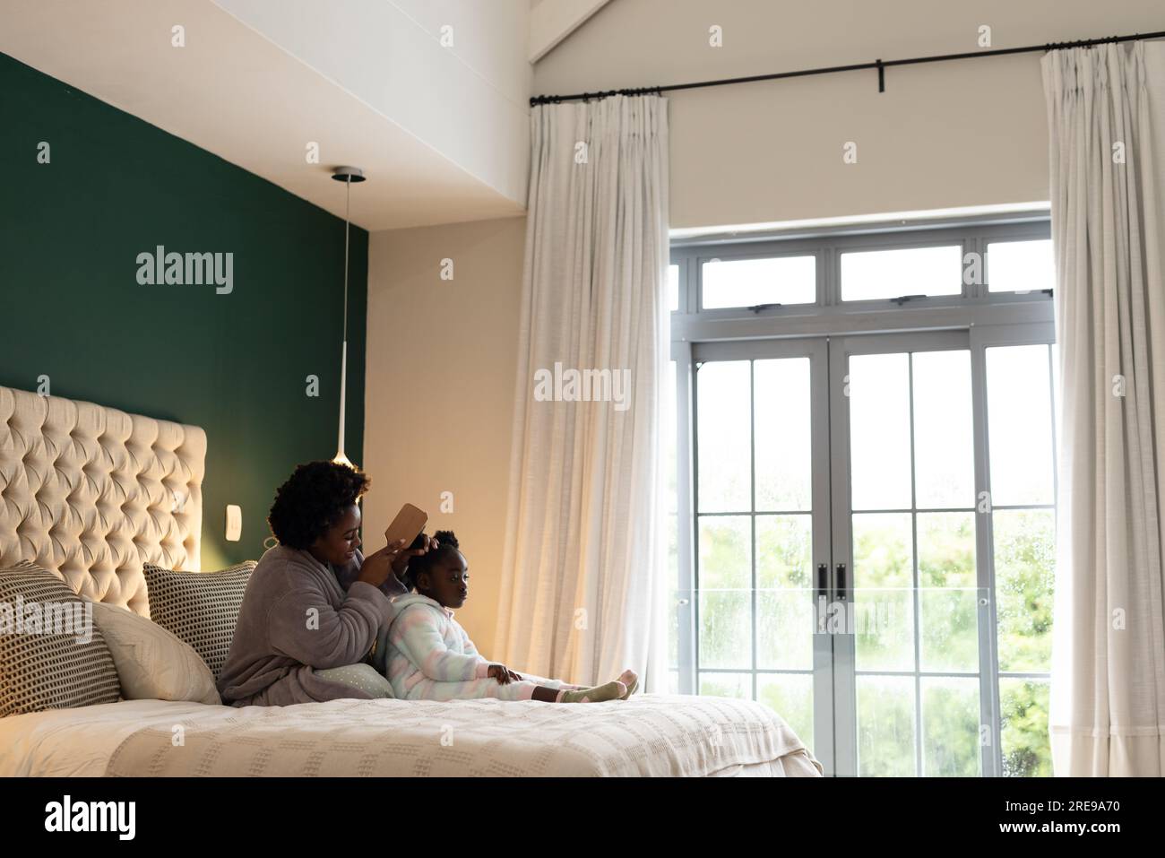 Glückliche afroamerikanische Mutter und Tochter sitzen auf dem Bett und bürsten zu Hause Haare, Kopierraum Stockfoto