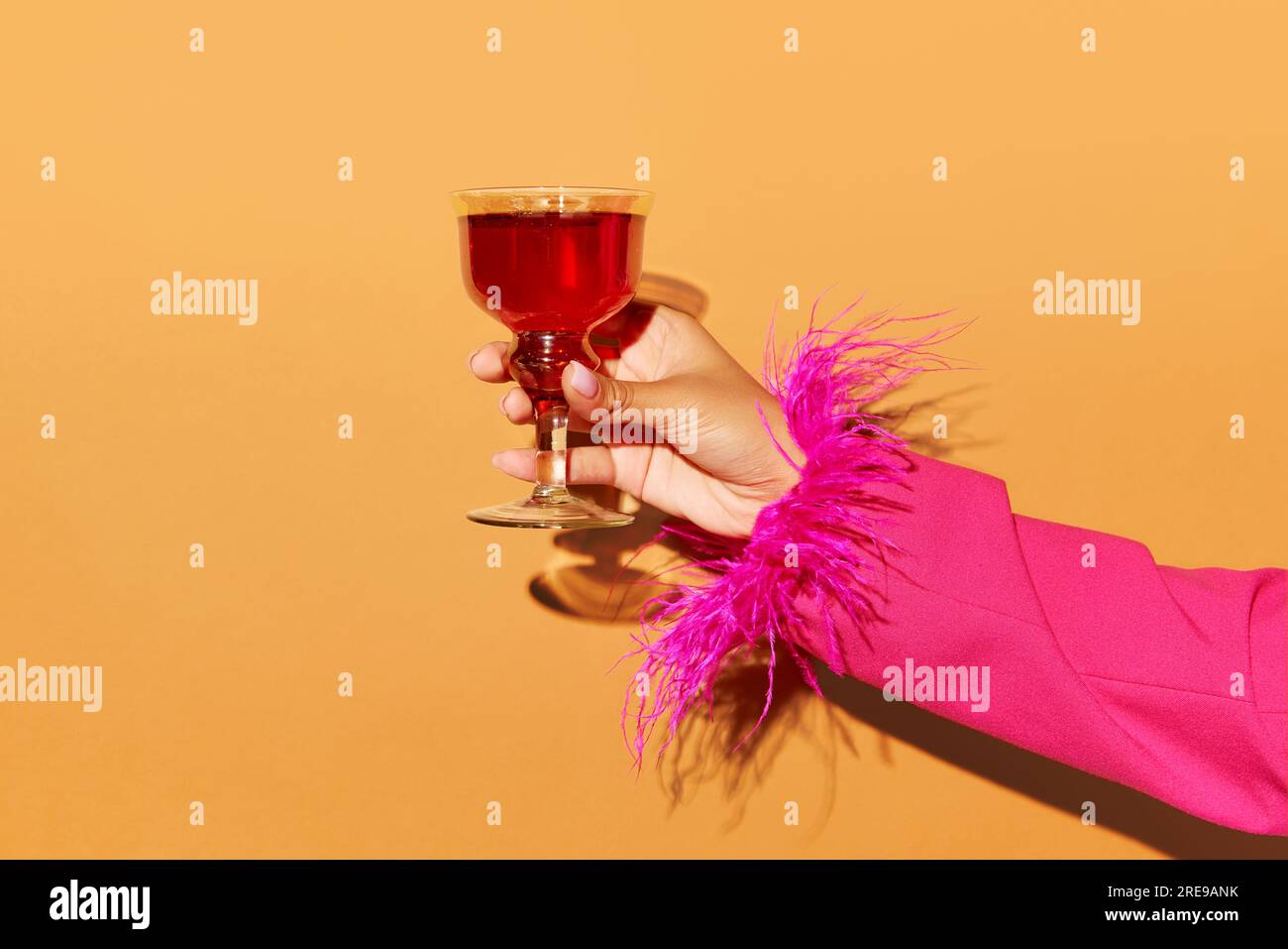 Handgehaltenes hohes Glas mit Rob Roy-Cocktail auf hellorangefarbenem Hintergrund. Werberaum. Stockfoto