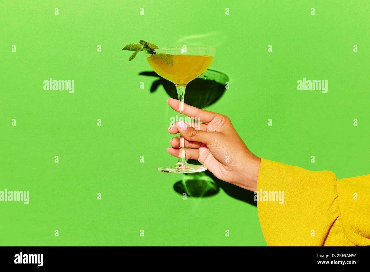 Handgehaltenes hohes Glas mit Rob Roy-Cocktail auf hellorangefarbenem Hintergrund. Werberaum. Stockfoto
