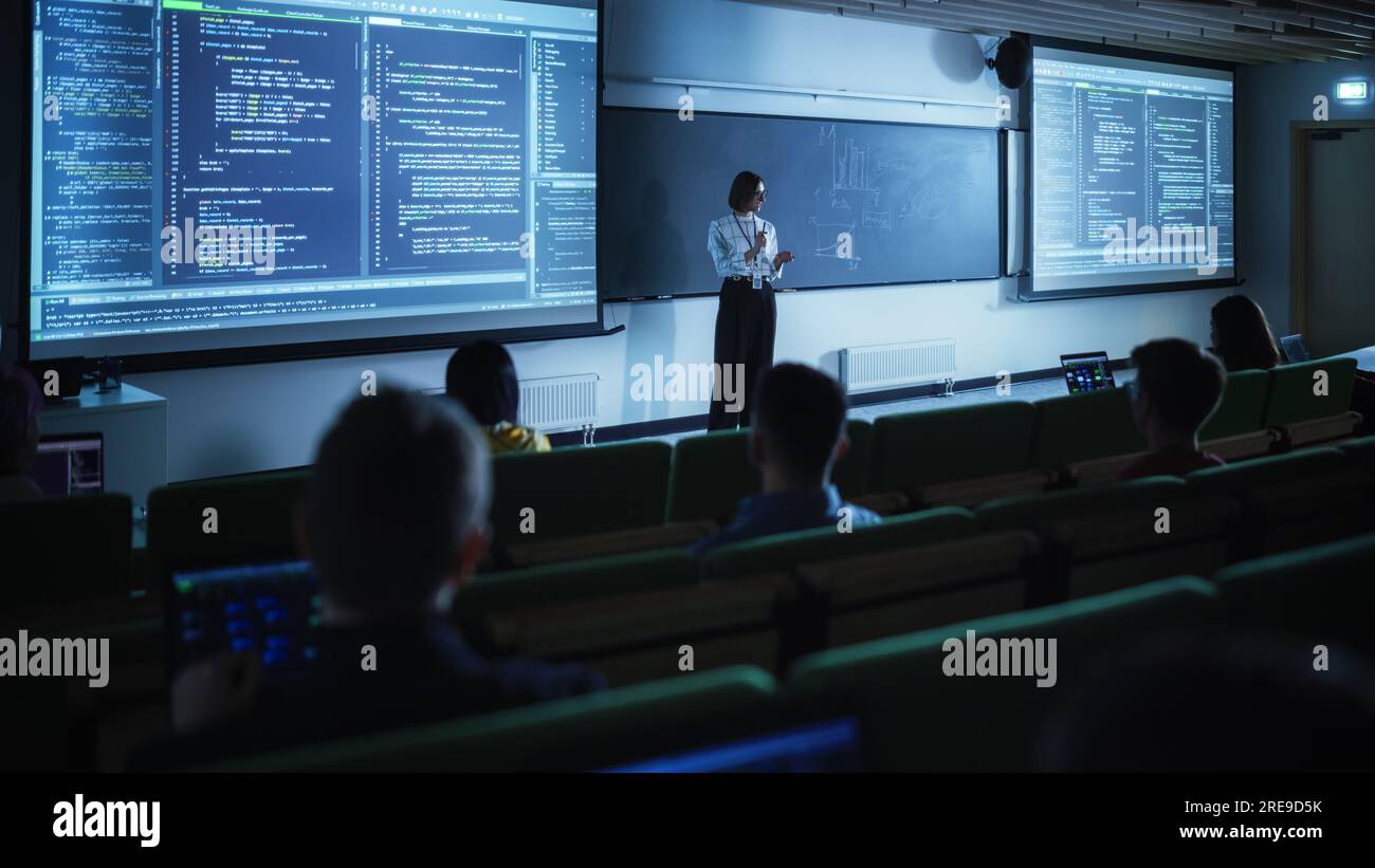 Junge Lehrerin, die eine Vorlesung zur Datenwissenschaft für verschiedene ethnische Gruppen von weiblichen und männlichen Schülern im Dark College Room hält. Diashow Wird Projiziert Stockfoto